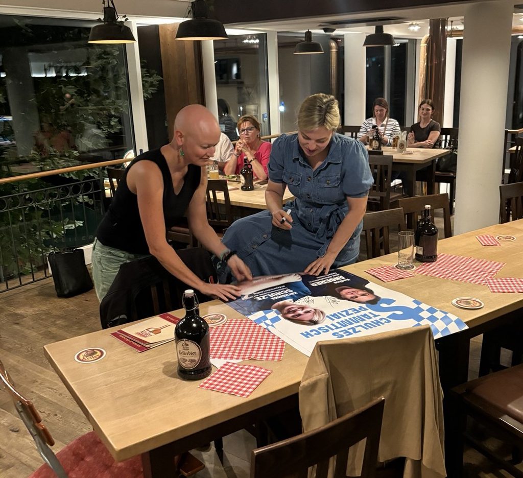 Katharina Schulze gibt ein Autogramm auf dem Veranstaltungsplakat - mit Lena Werner